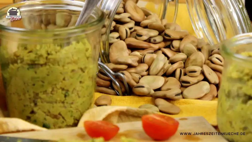 Scharf im Hintergrund getrocknete Ackerbohnen, Im Vordergurnd ein Glas mit Ackerbohnenaufstrich