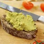 Eine Scheibe Schwarzbrot, die mit Ackerbohnenaufstrich bestrichen ist