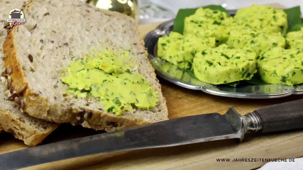 Neben Brotscheiben liegt auf einem silbernen Teller Bärlauchbutter.