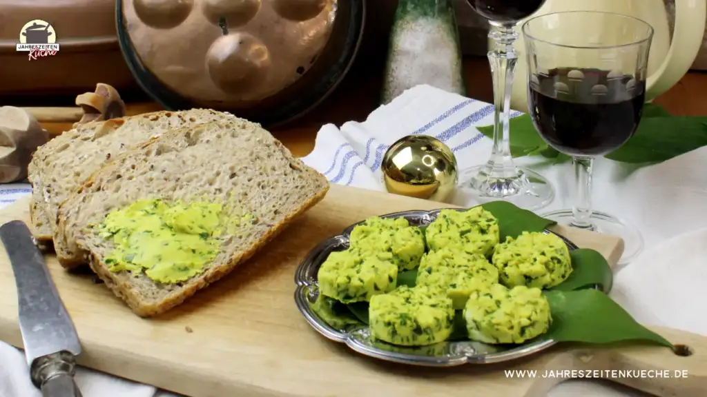 Neben Brotscheiben liegt auf einem silbernen Teller Bärlauchbutter. Dahinter ist eine goldene Kugel