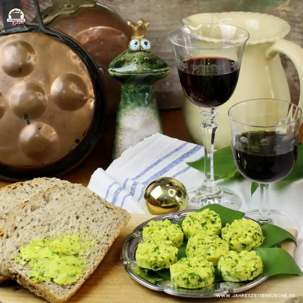 Alte Küchenuntensilien und der Froschkönig im Hintergrund. Im Vordergrund ein Teller mit Bärlauchbutter und Brotscheiben
