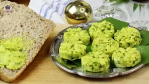 Neben Brotscheiben liegt auf einem silbernen Teller Bärlauchbutter. Dahinter ist eine goldene Kugel