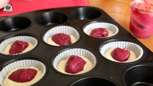 Muffinförmchen, die halb mit Teig und Brombeer Curd gefüllt sind