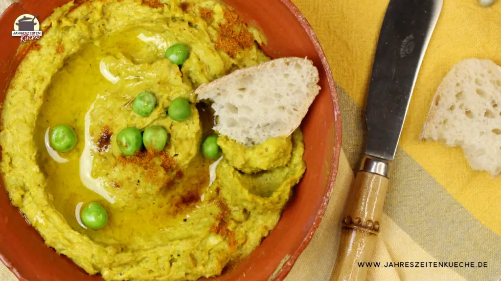 Erbsenhummus in einer Schale mit Olivenöl und Weißbrot angerichtet