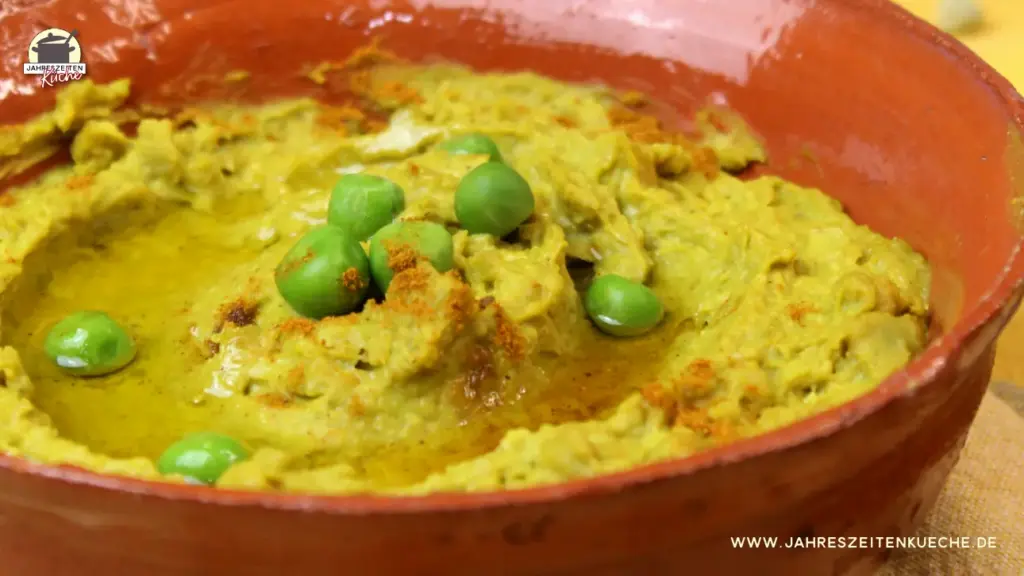 Erbsenhummus in einer Schale mit Olivenöl und frischen grünen Erbsen garniert