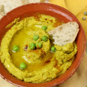 Erbsenhummus in einer Schale mit Olivenöl und Weißbrot angerichtet