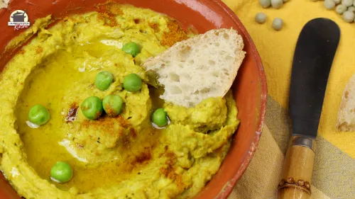 Erbsenhummus in einer Schale mit Olivenöl und Weißbrot angerichtet