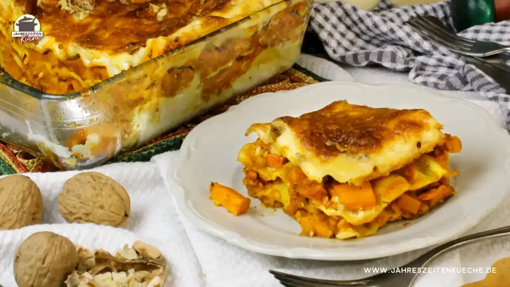 Im Vordergrund ein Teller mit einem Stück Kürbis-Lasagne, Dahinter steht eine Auflaufform aus Glas mit frisch gebackener Kürbis-Lasagne